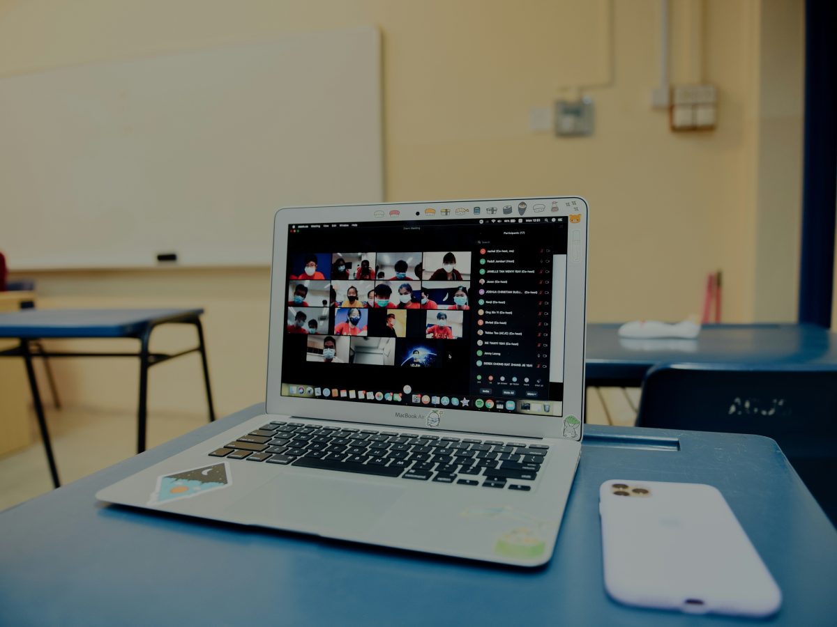 Laptop on a desk, on the screen is a virtual meeting with students.