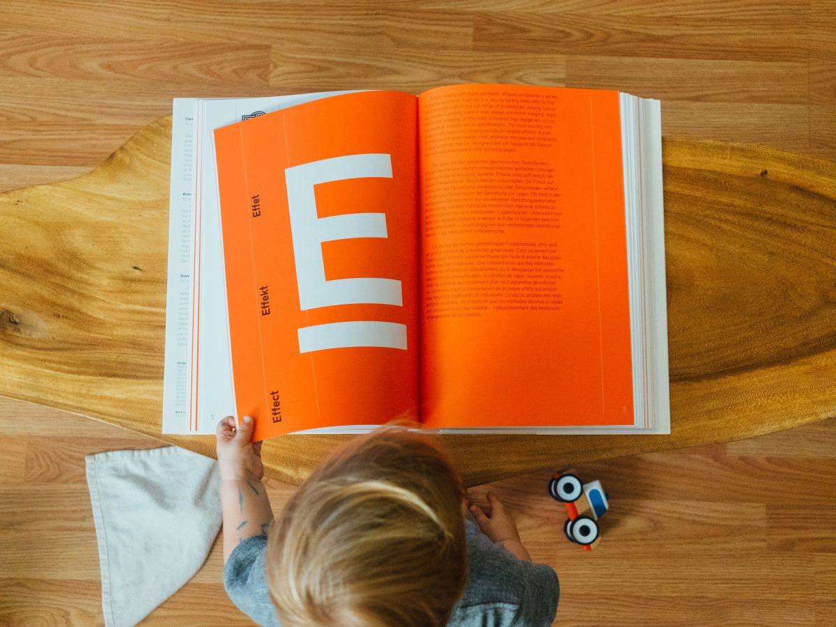 Person open a bright orange education book, with letter E. Credit to Paul Hanaoka.