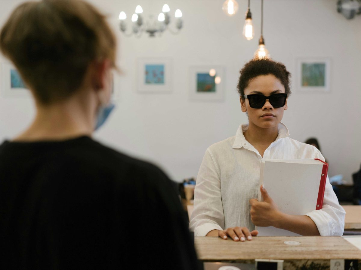 Woman wearing sunglasses holding a book is faced towards the camera